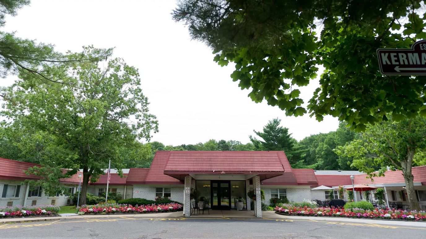 Front entrance of a senior living facility surrounded by gardens