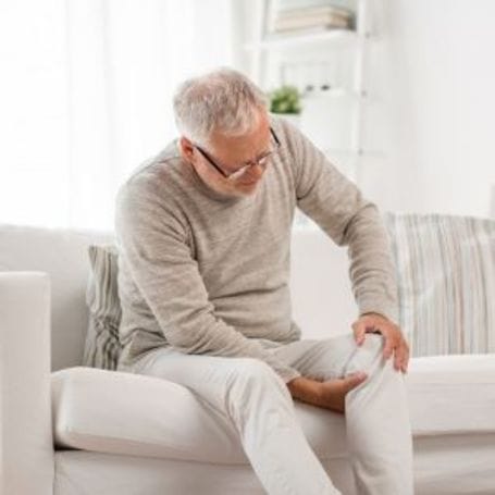 Senior man sitting on a couch, holding his knee