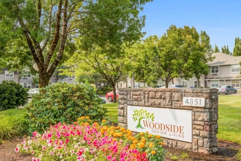 Exterior signage of Woodside Senior Living with surrounding flowers