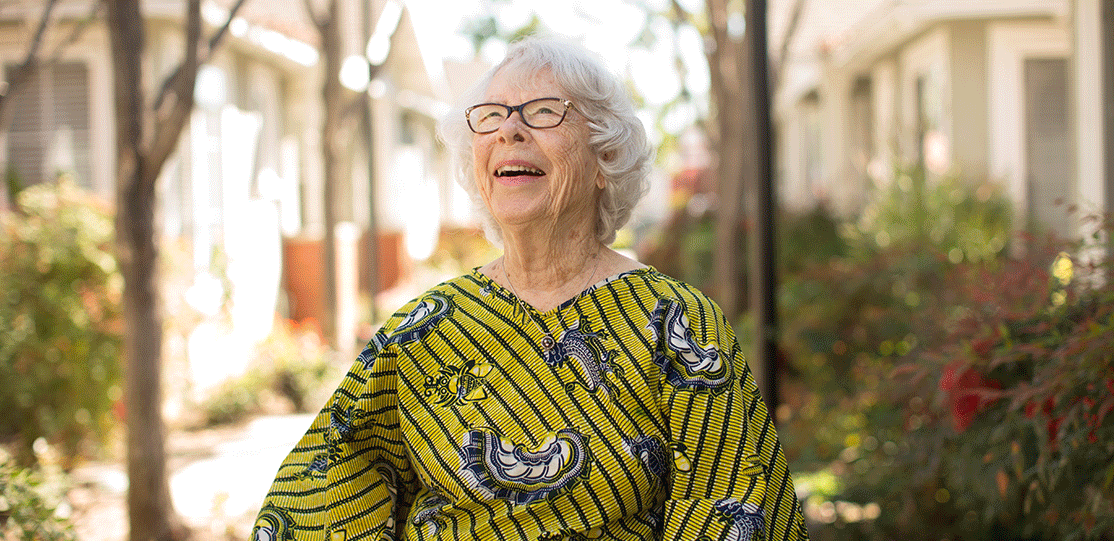 A smiling elderly woman in a colorful dress outdoors