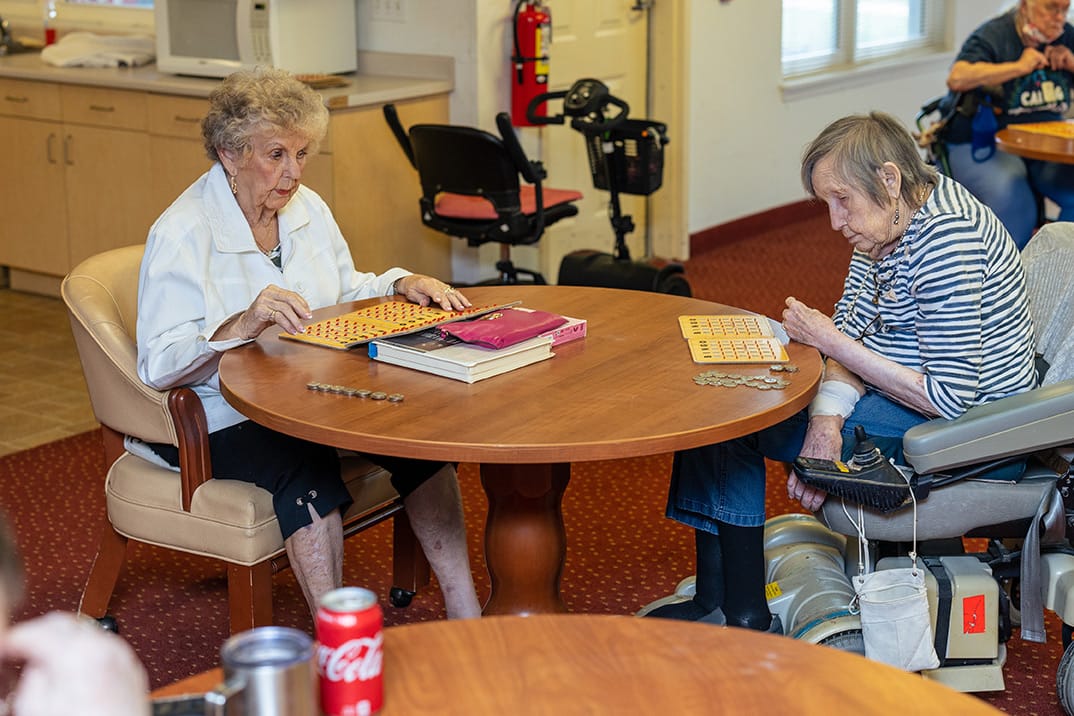 Residents playing bingo at a large table in a common area