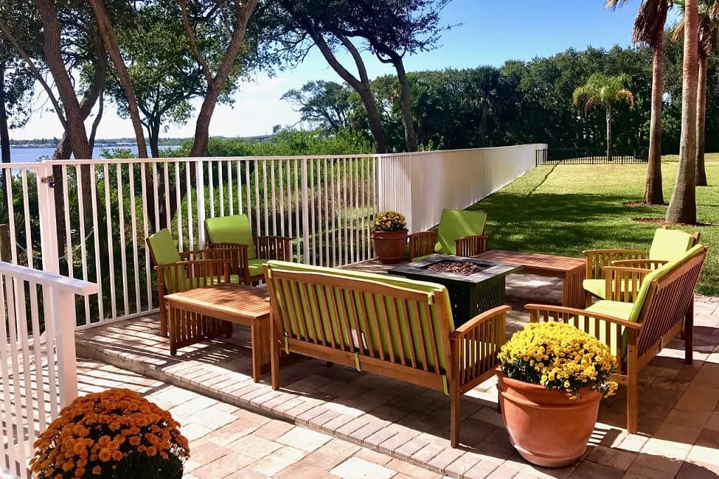 Cozy outdoor seating area with green chairs and flowers overlooking a garden.