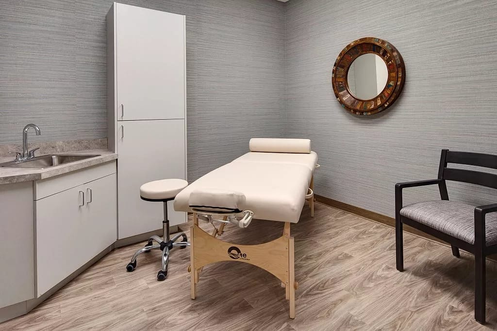 A clean therapy room featuring a treatment table, a sink, and a chair.