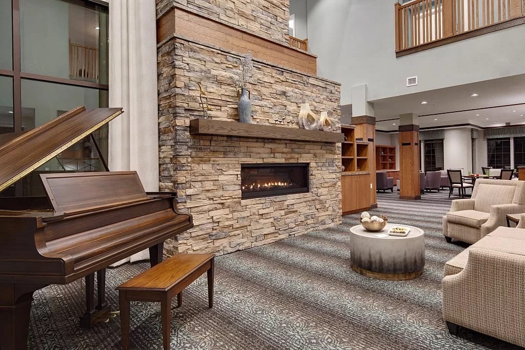 Warm and inviting lobby with a piano, stone fireplace, and comfortable seating.