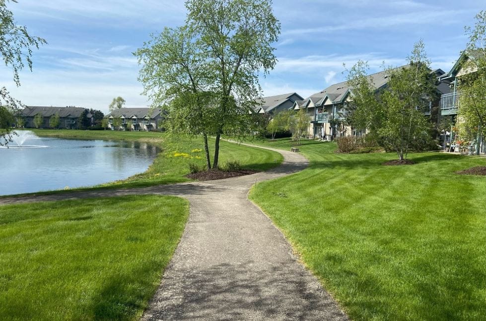 Pathway winding around a pond with green lawns and residential buildings