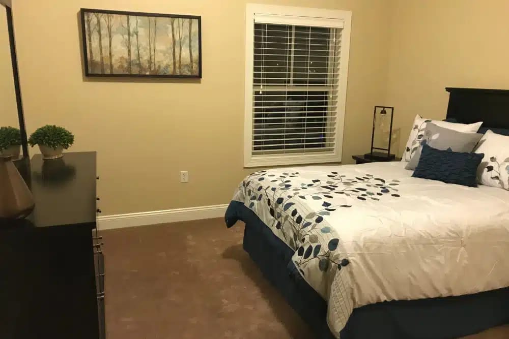A spacious bedroom featuring a bed, dresser, and window.