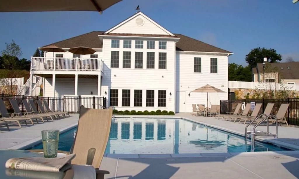 Poolside view of Newbury Village with lounge chairs and a white building in the background.
