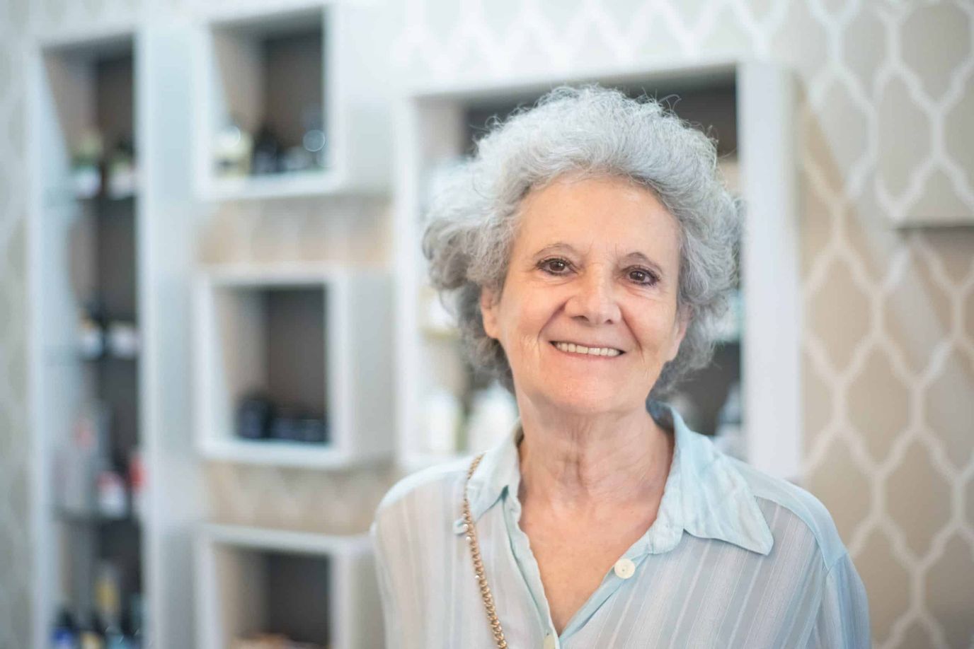 A smiling elderly woman indoors, possibly at a salon