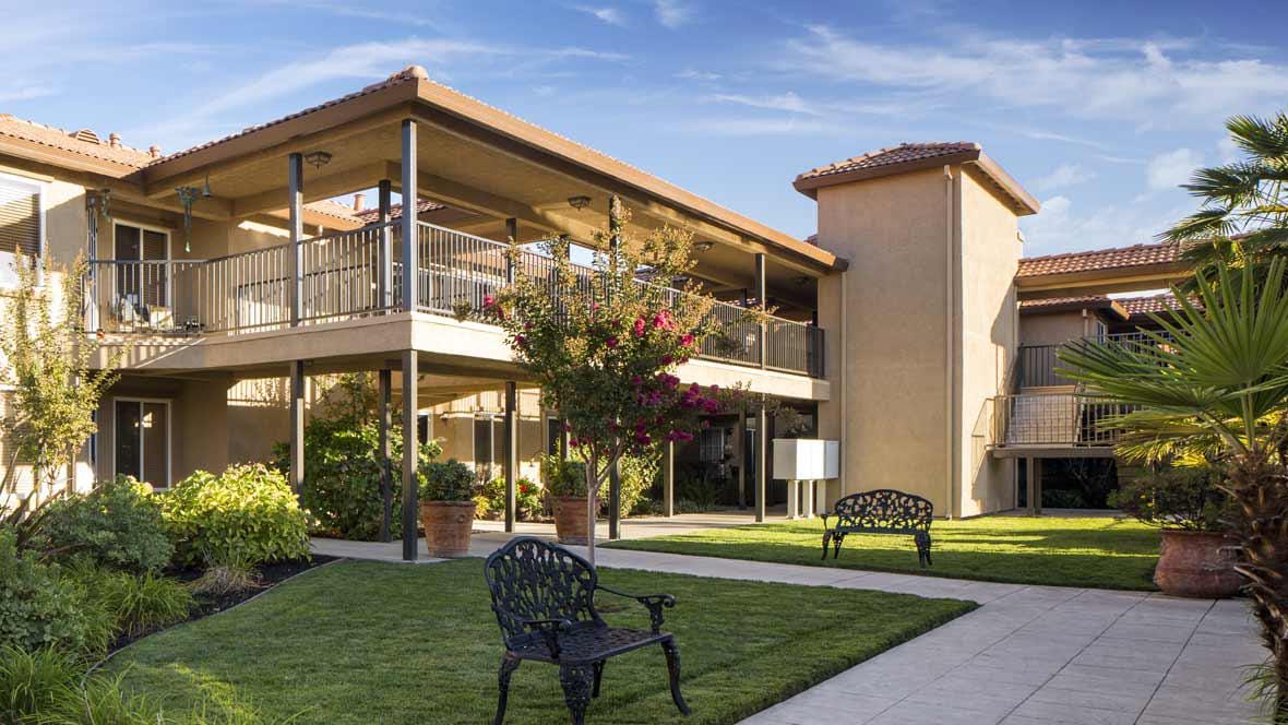 Exterior view of a senior living facility with gardens and seating