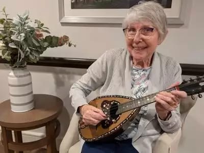 Senior woman playing a mandolin in a common area.