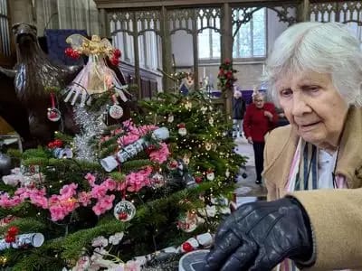 Elderly woman admiring a decorated Christmas tree.