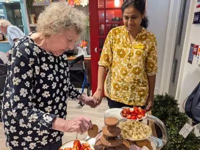 Resident enjoying fondue with staff assistance.