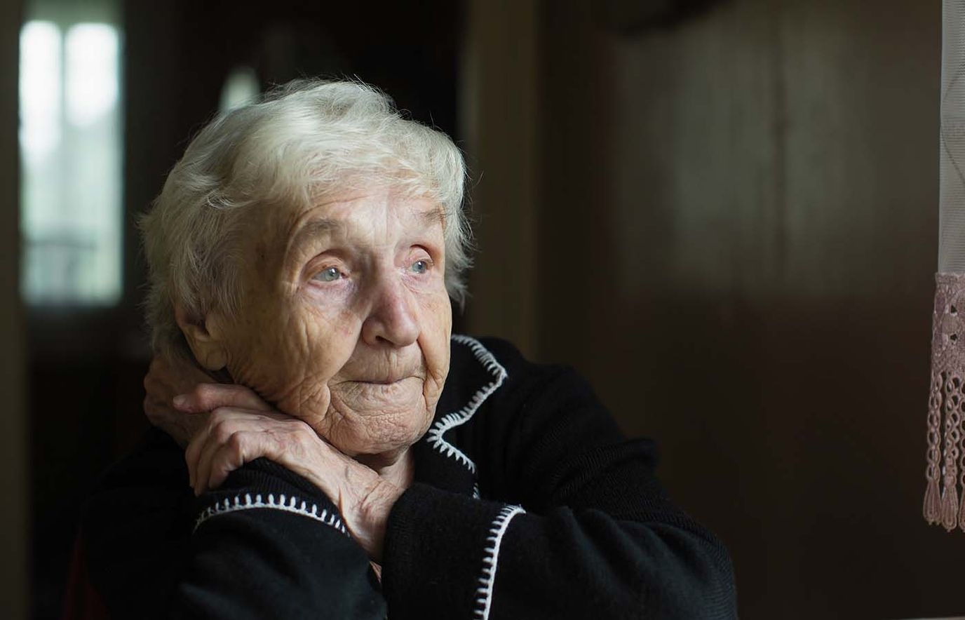 An elderly woman looking thoughtfully out a window