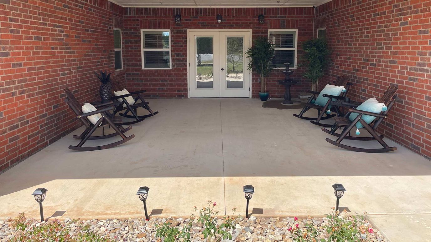BeeHive Homes of Granbury, assisted living in Granbury, TX — Covered outdoor seating area with rocking chairs and plants