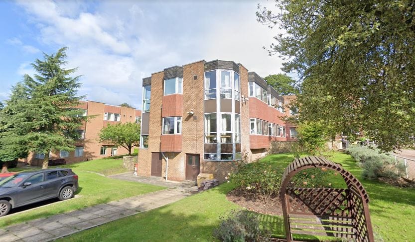 Exterior view of Alderbrook Care Home with trees and parking