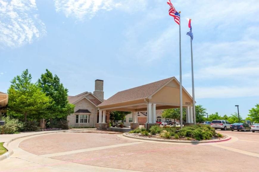 Entrance of Ellery Arbor Memory Care with flags and landscaped area