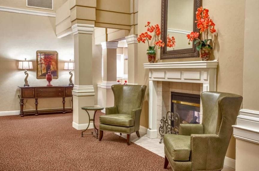 Comfortable green chairs near a fireplace adorned with flowers