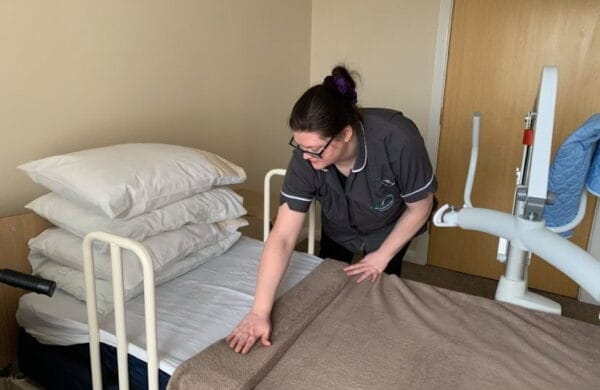 Staff member smoothing a blanket on a bed in a senior living facility