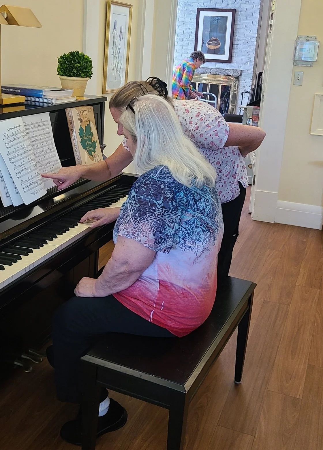Two women playing piano together in a shared space.