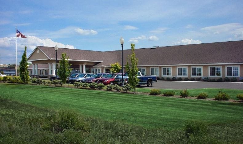Exterior view of the assisted living facility with landscaping and vehicles