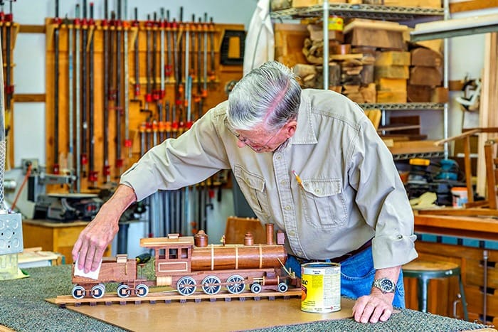 A resident working on a wooden train model in a workshop