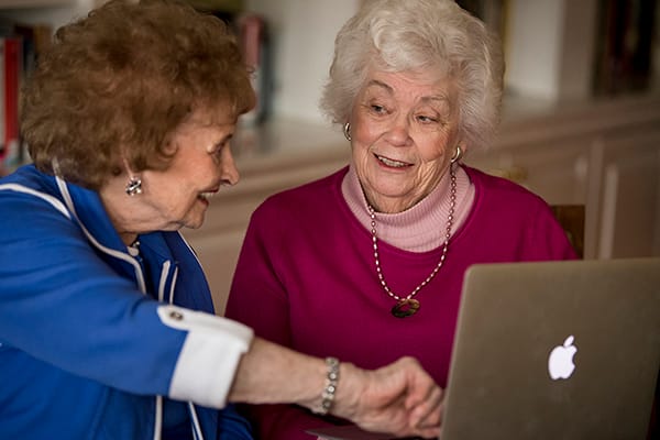 Two elderly women interacting with a laptop in a cozy setting