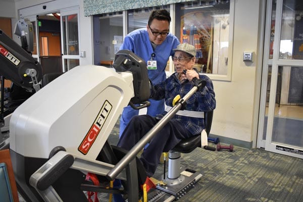Resident and staff using exercise equipment in therapy room