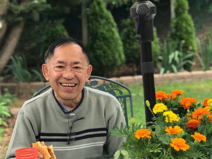 Elderly man smiling with food and flowers in garden