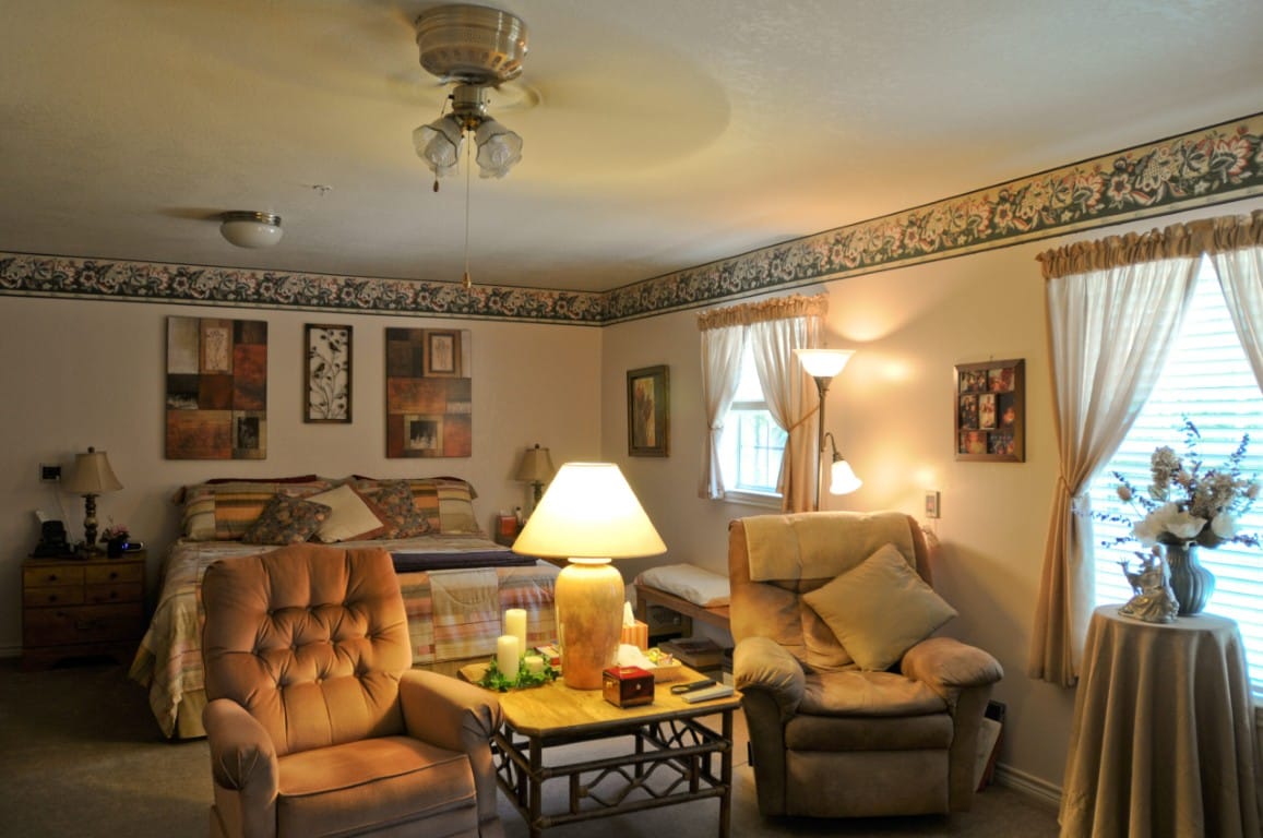 A well-furnished bedroom featuring a bed, two chairs, and decorative art on the walls.