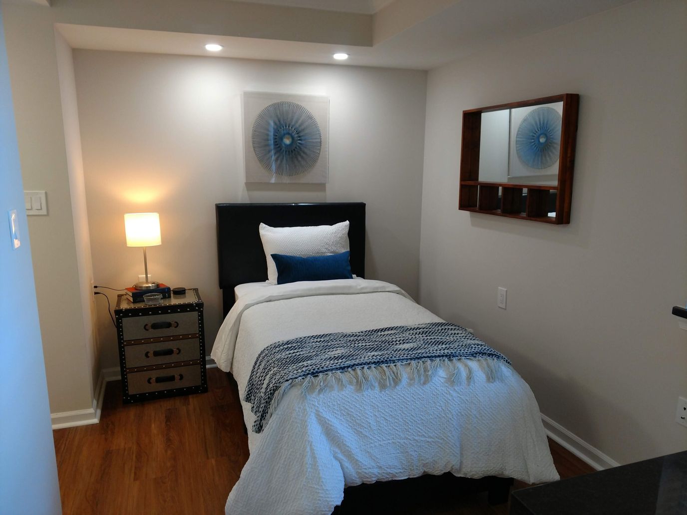 A serene bedroom with a single bed, lamp, and decorative wall art.