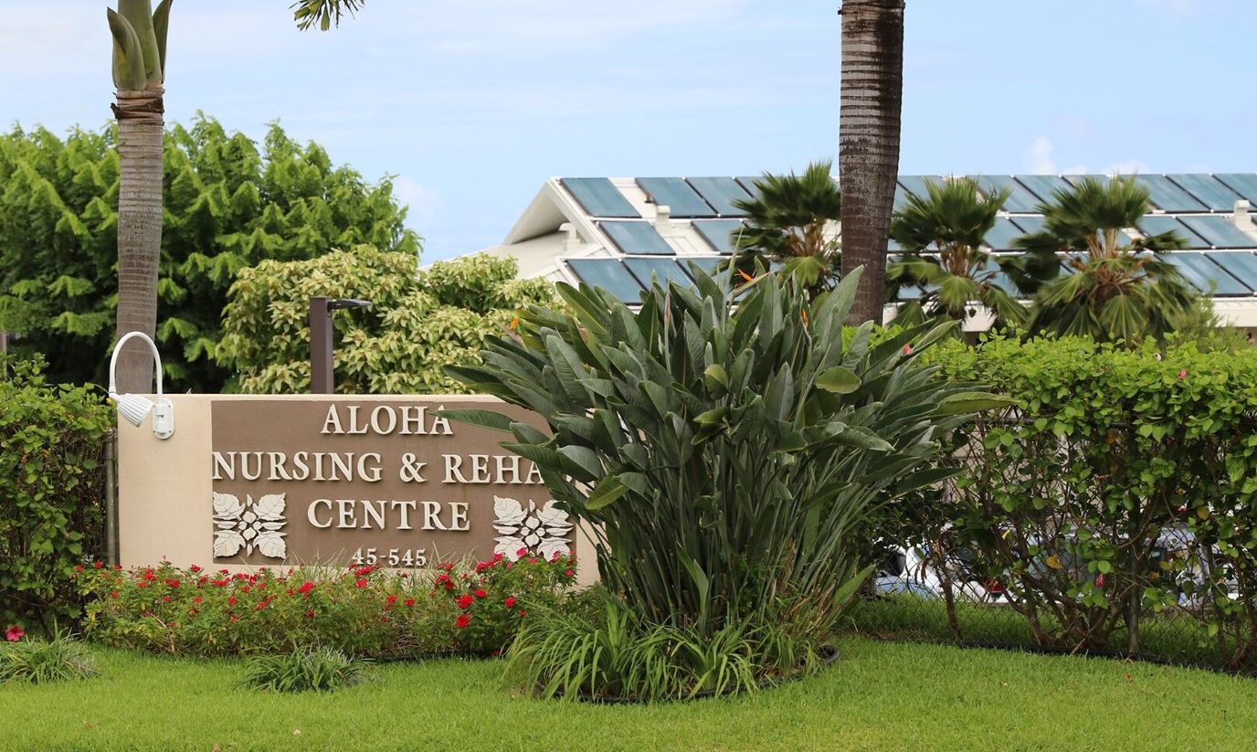 Signage for Aloha Nursing and Rehab Center surrounded by greenery