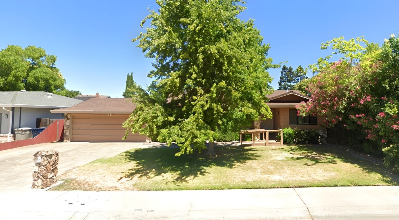 Exterior view of a single-story house with a large tree