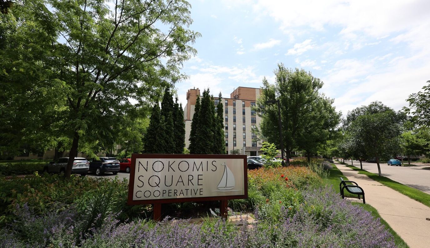 Sign for Nokomis Square Cooperative with gardens and building in background