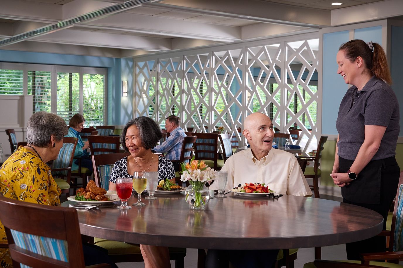 Residents enjoying meals in the dining room with staff interaction