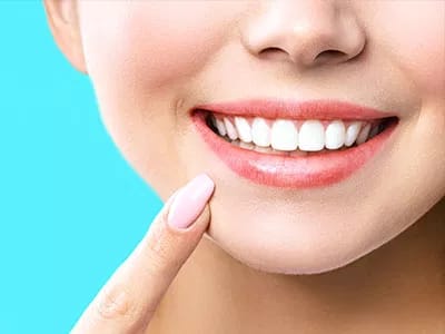 Arabella Health & Wellness of Phenix City, Nursing Home in Phenix City, AL — Smiling woman pointing at her teeth against a blue background