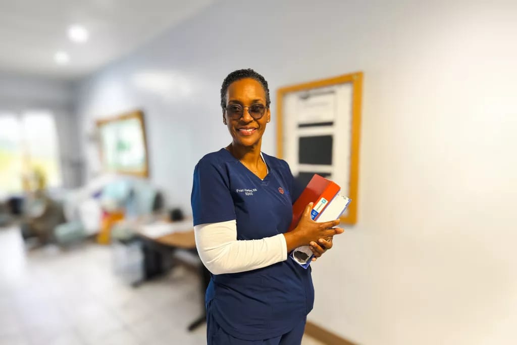 Arabella Health & Wellness of Phenix City, Nursing Home in Phenix City, AL — Nurse holding medical supplies in a living facility hallway
