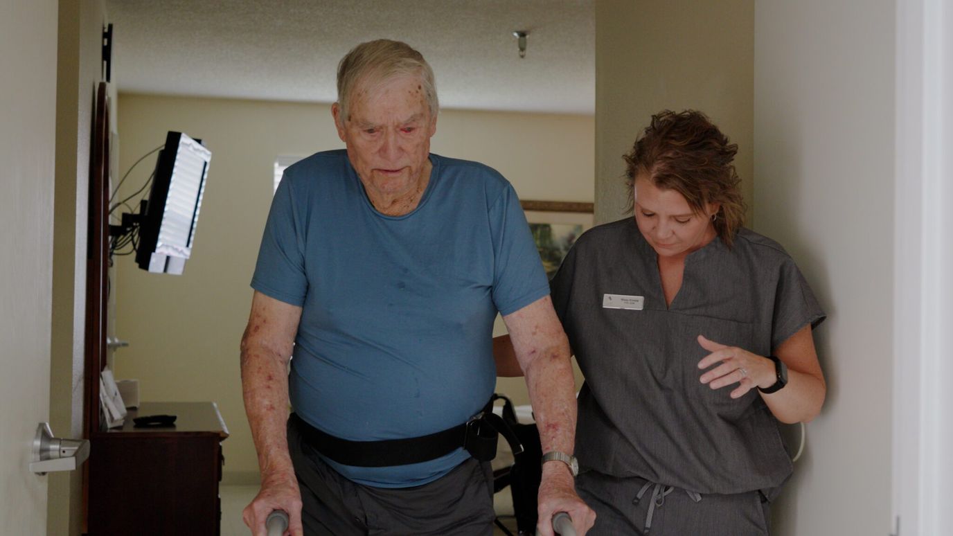 A senior man with a walker assisted by a caregiver