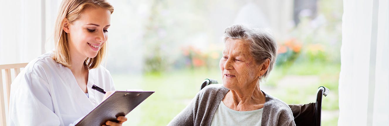 A caregiver interacting with an elderly woman in a bright indoor space