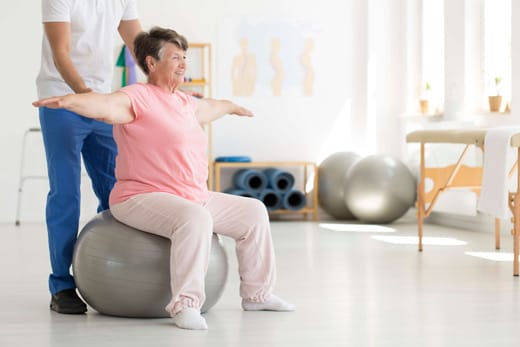 Elderly woman exercising on a stability ball with assistance