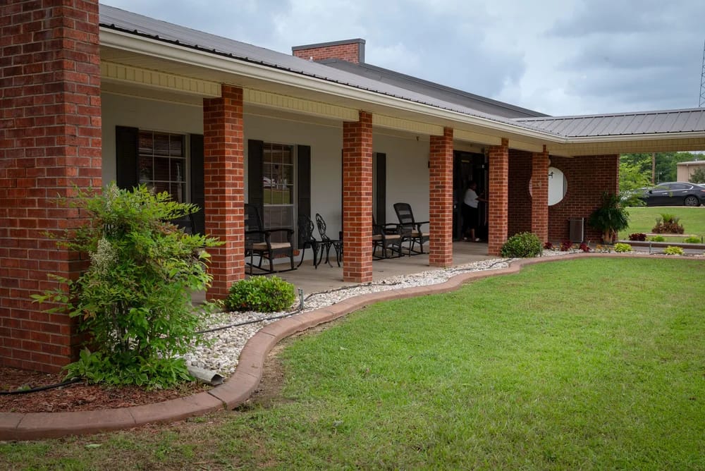 Exterior view of a brick nursing home entrance with rocking chairs