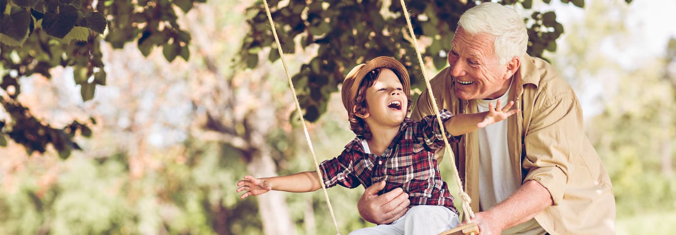 Grandfather playing on a swing with a child in a park