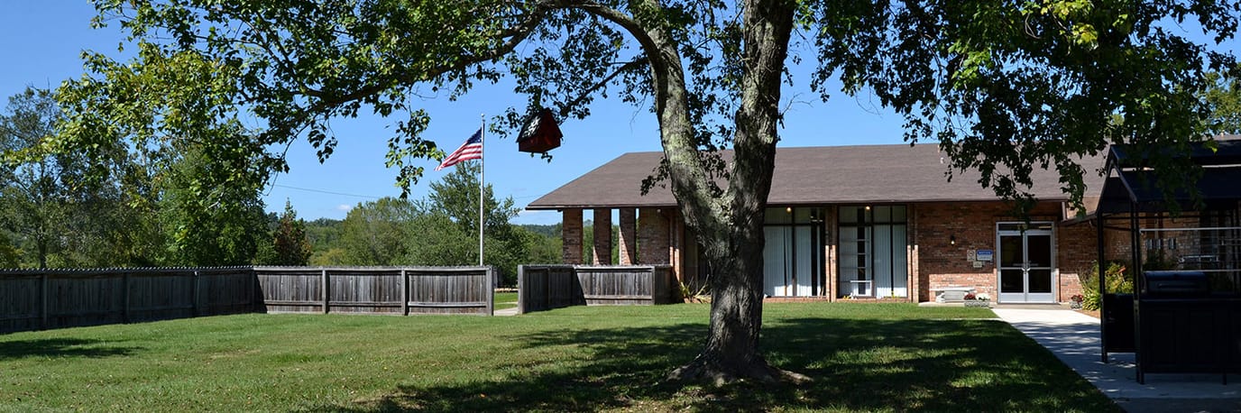 Exterior view of a senior living facility with a tree and flag