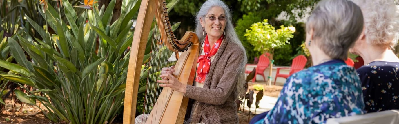 Resident playing harp outdoors for engaged audience
