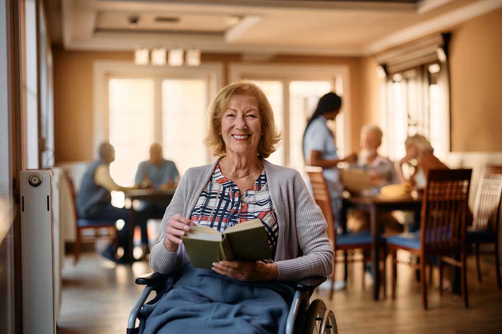 Resident reading in a common area with staff in the background