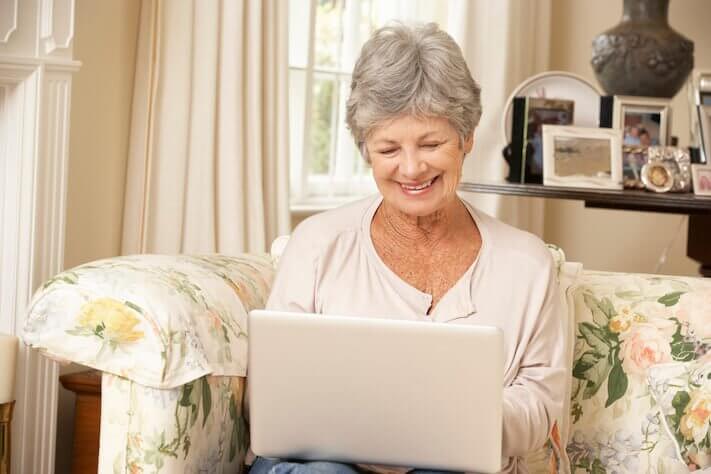 Arbor Terrace at Cascade, memory care in Atlanta, GA — Smiling senior woman using a laptop on a sofa