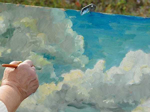 Close-up of a hand painting a cloudy sky