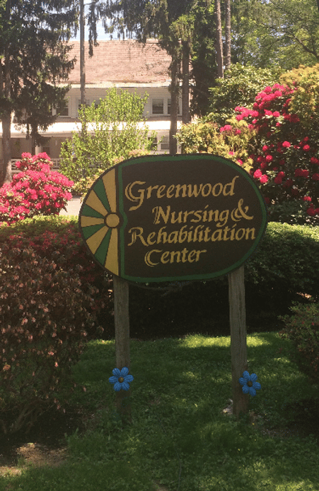 Signage for Greenwood Nursing & Rehabilitation Center surrounded by flowers