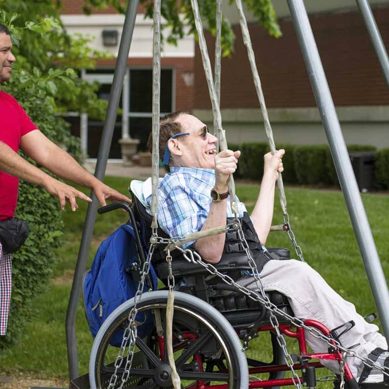 Resident enjoying a swing in the garden with staff assistance