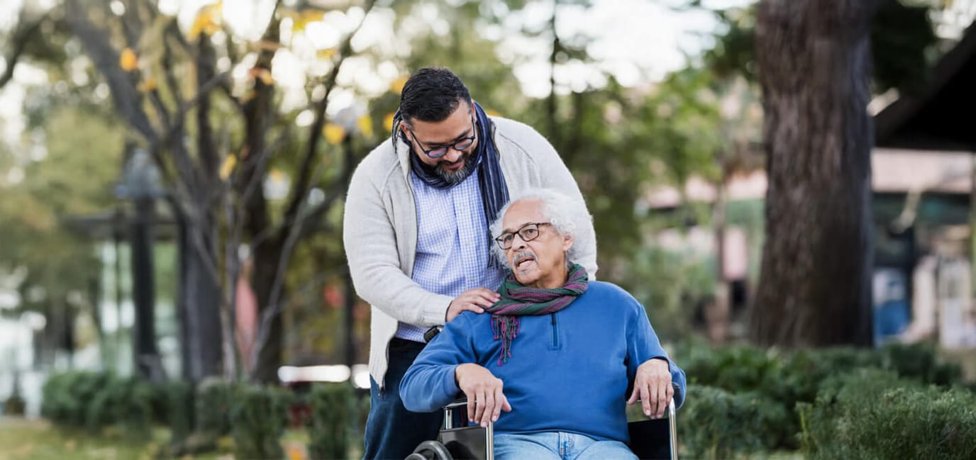 Caregiver assisting an older man in a wheelchair in a garden