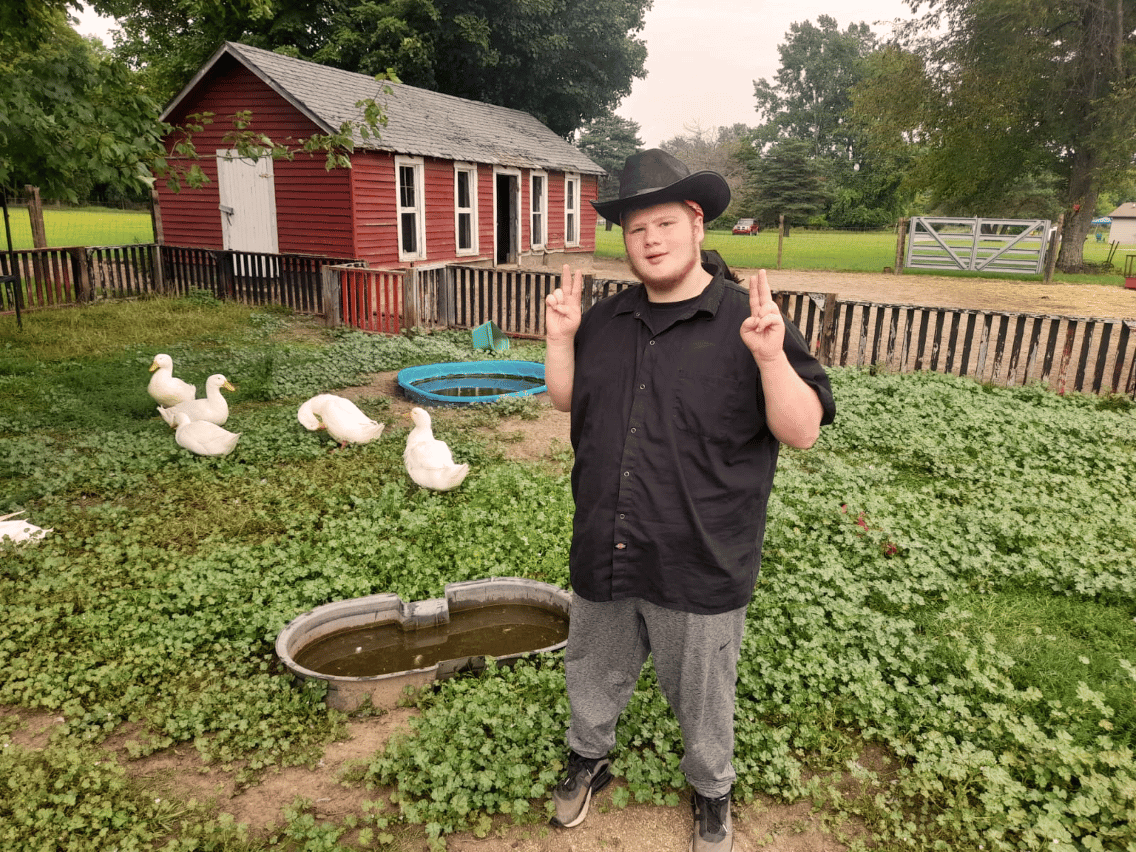 A young man with ducks by a red building.